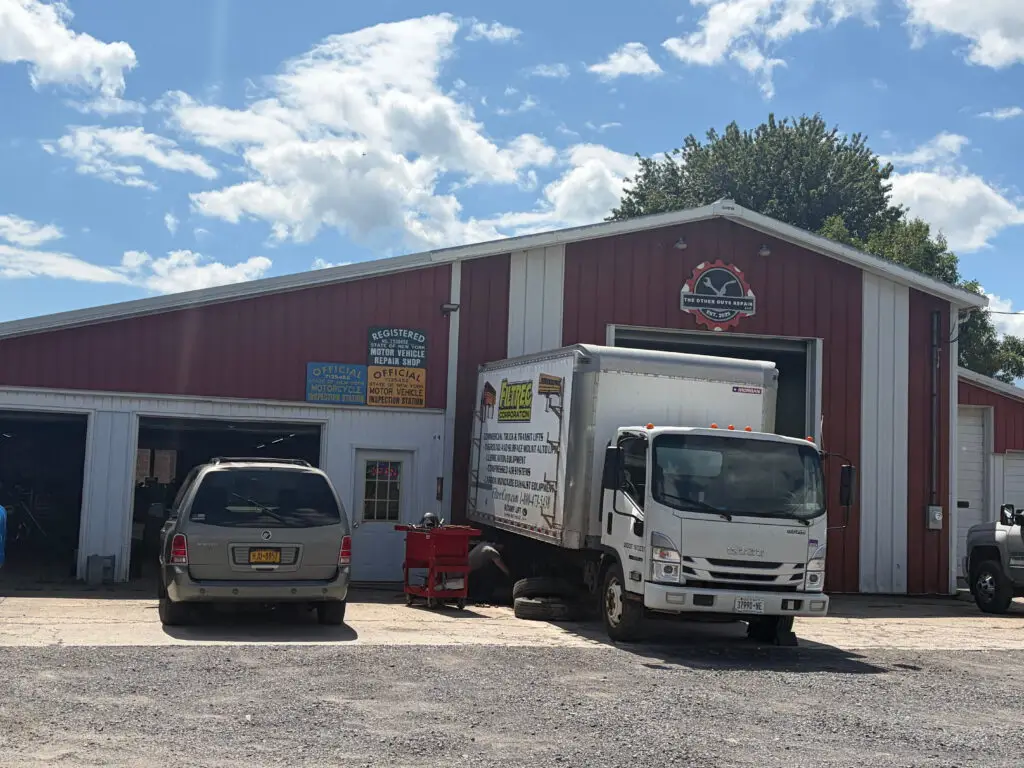 The Other Guys Repair shop in Cayuga, NY, with three open service bays and vehicles parked outside