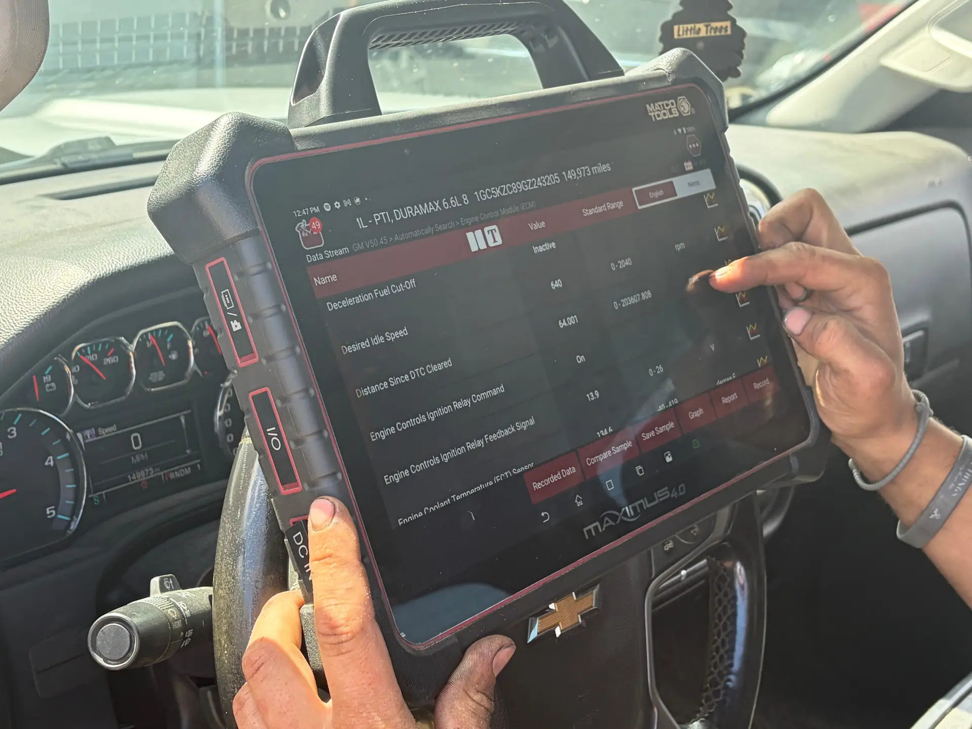 A technician reading live engine data on a diagnostic scanner in a Duramax diesel truck at The Other Guys Repair